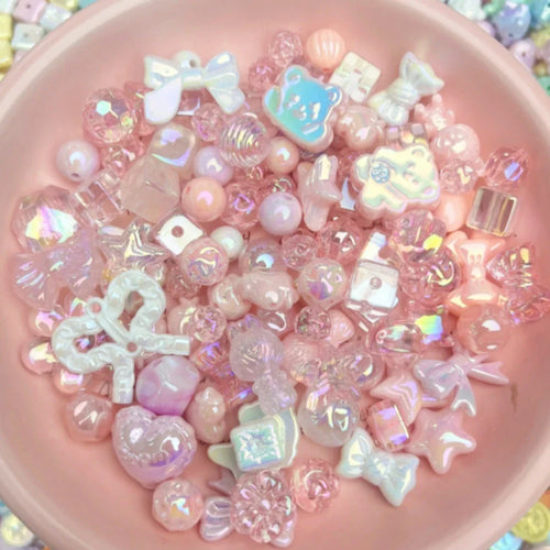 A pink bowl filled with an assortment of iridescent pink, white, and clear craft beads in shapes like bows, hearts, and