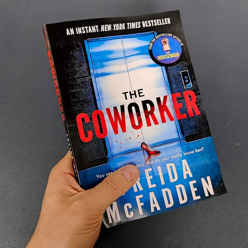 A physical copy of the thriller book The Coworker by Freida McFadden being held in a hand.
