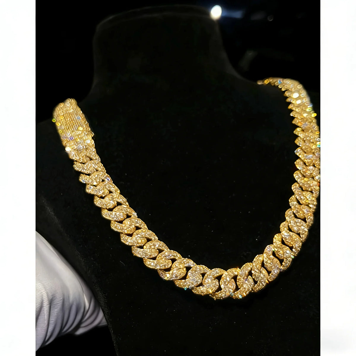 Men's heavy gold tone Cuban link chain necklace with sparkling moissanite stones on a black display bust