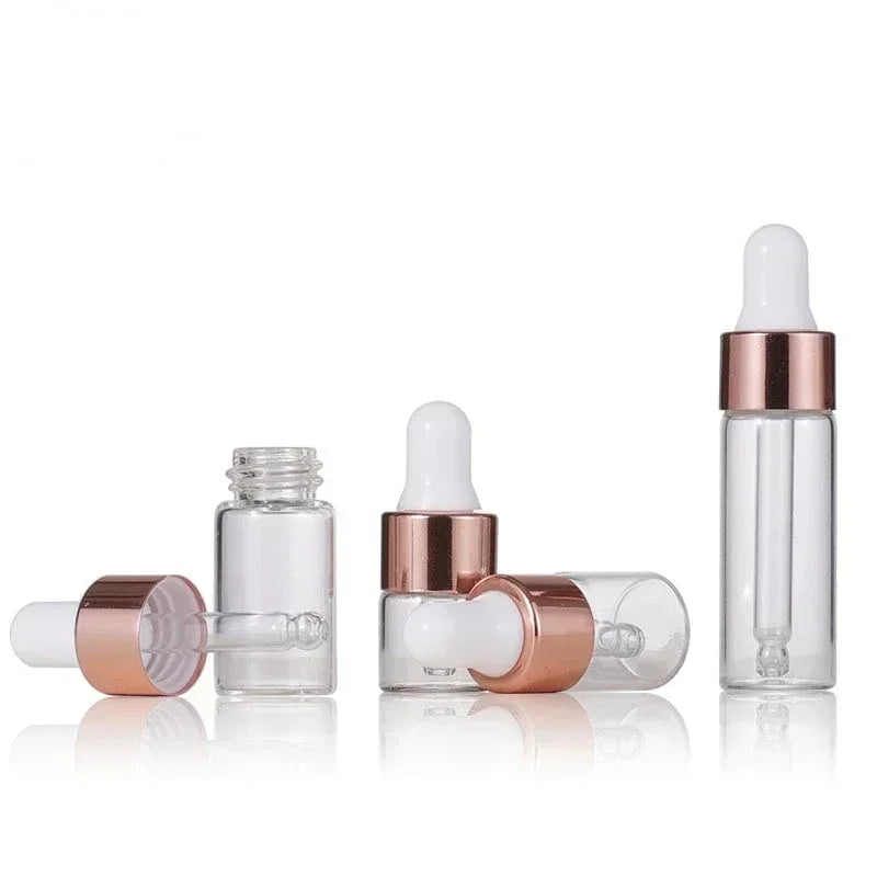 A set of clear mini glass dropper bottles with rose gold caps and white silicone droppers, arranged in various positions.