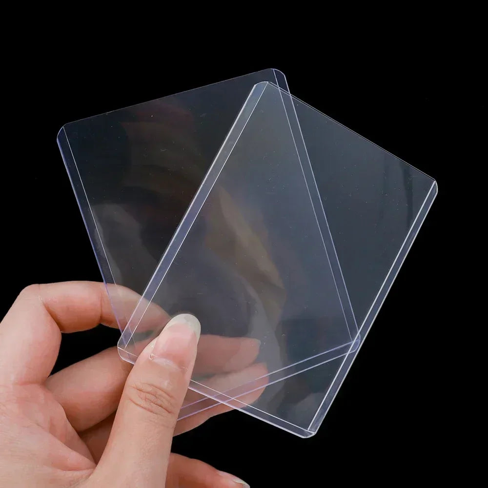 Person holding two clear rigid plastic protective card sleeves