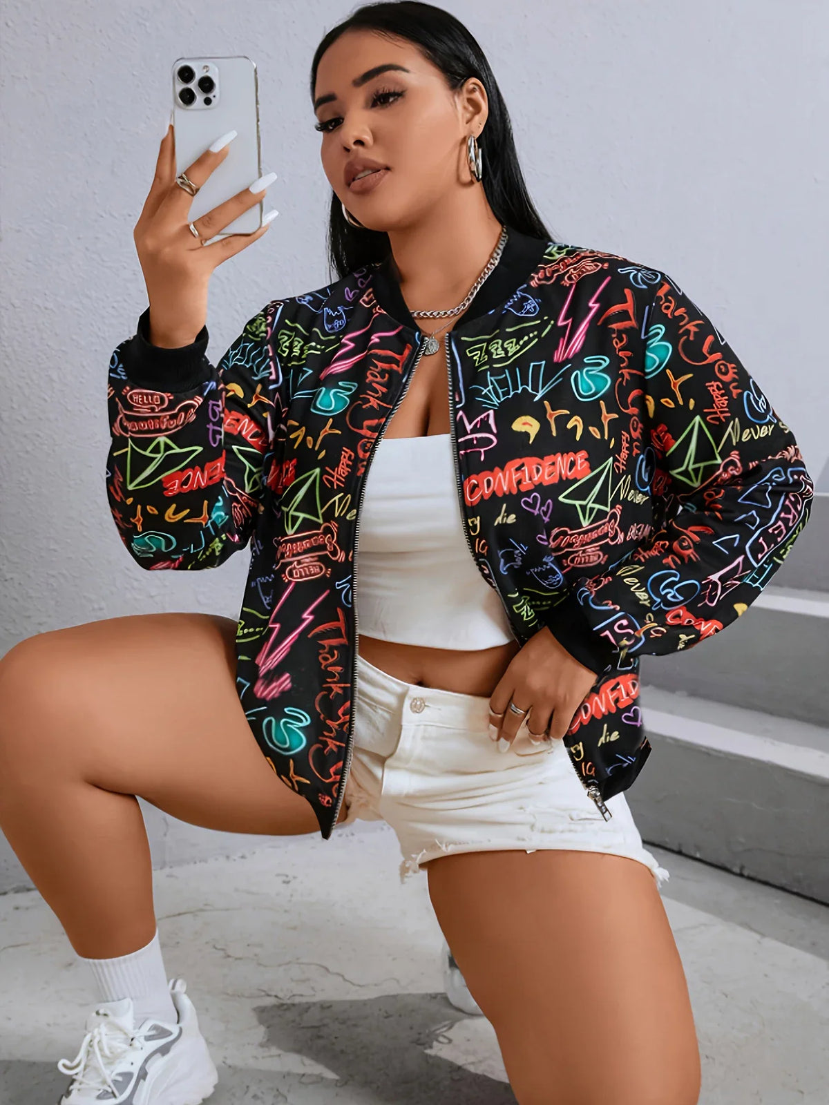 Plus size woman taking a selfie in a mirror wearing a colorful graffiti print zip-up bomber jacket.