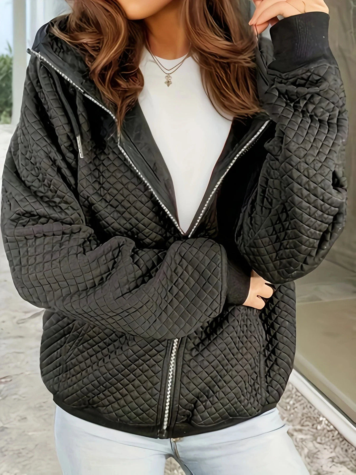A black diamond-quilted zip-up hooded jacket with ribbed cuffs, worn over a white shirt.