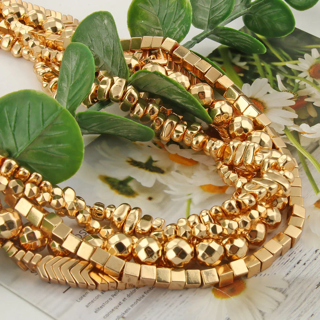 Assorted gold-plated metal beads arranged on top of leaves and paper with text.