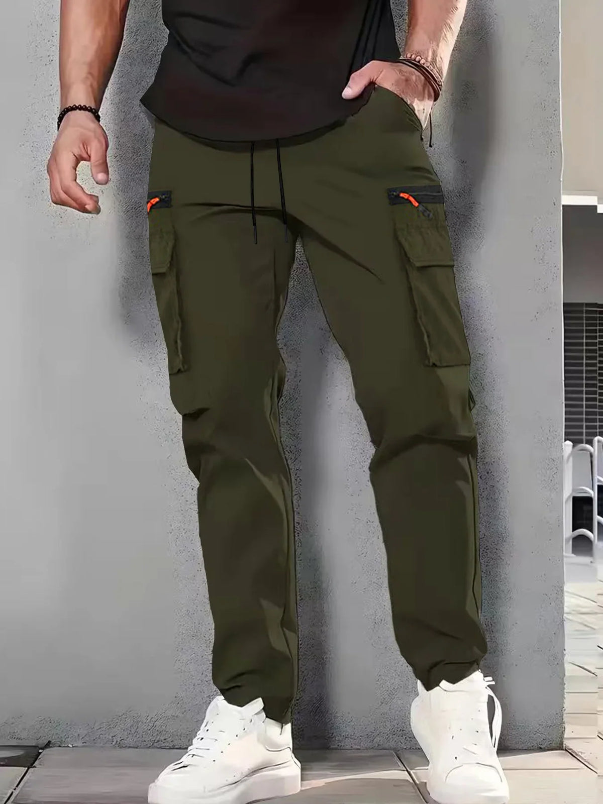 Man wearing olive green cargo pants with black zipper pockets and white sneakers.