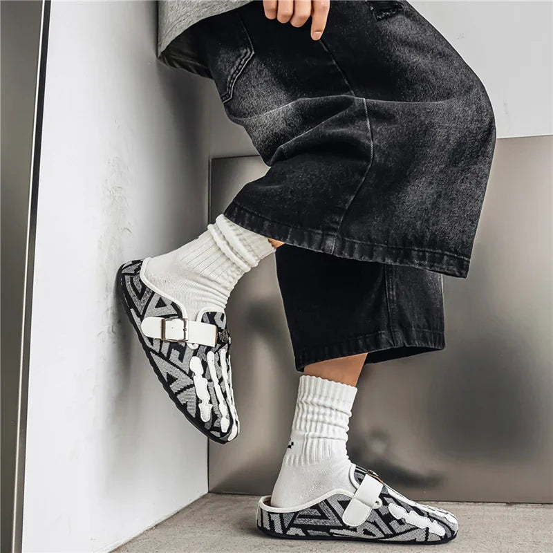 Men's black and white patterned slip-on mule shoes worn with white socks and wide-leg black trousers