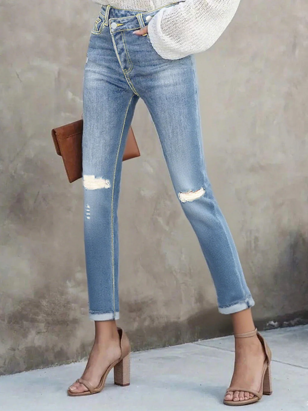 High-waisted light blue distressed skinny jeans with a crossover button fly