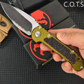 A hand holding a serrated folding pocket knife with an olive green handle and black textured grip.