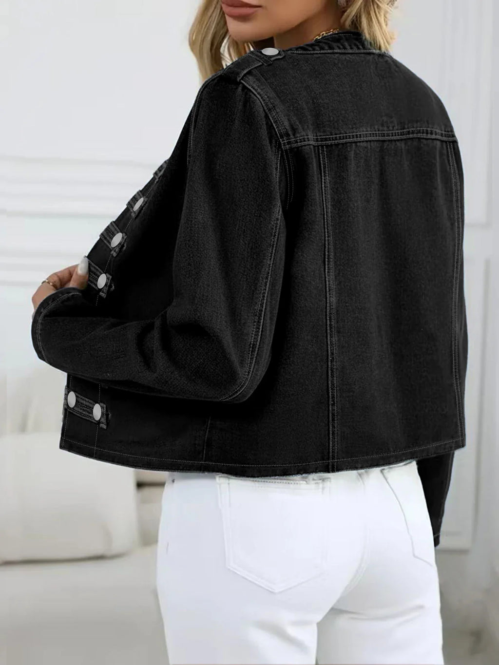 Back view of a woman wearing a black washed denim jacket with white jeans