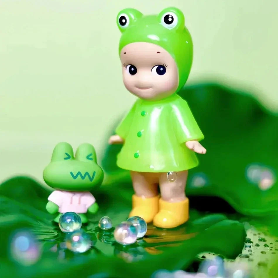 Small collectible doll figurine in a green frog hat and raincoat with a toy frog