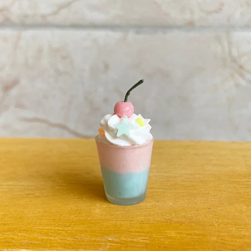 A single miniature dessert cup with pink and blue layers, whipped cream, star sprinkles, and a cherry topper.