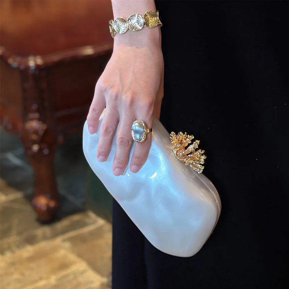 White marbled acrylic evening clutch with gold coral-shaped clasp held by a woman