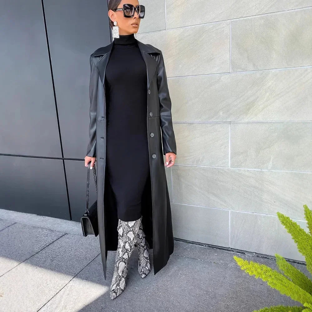 A woman wearing a black leather trench coat over a black dress and snake print boots.