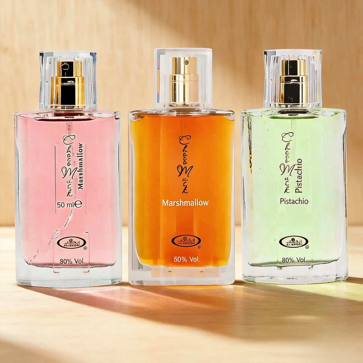 Three 50ml perfume bottles in pink, orange, and light green standing on a wooden surface in warm sunlight.