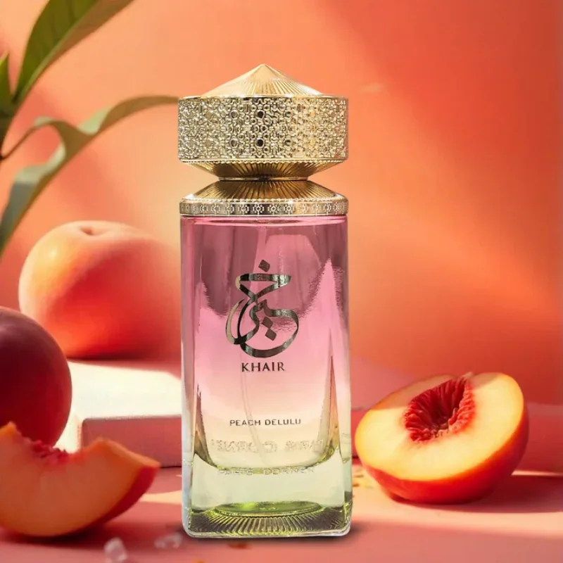 A glass perfume bottle with a golden cap surrounded by fresh peach halves.