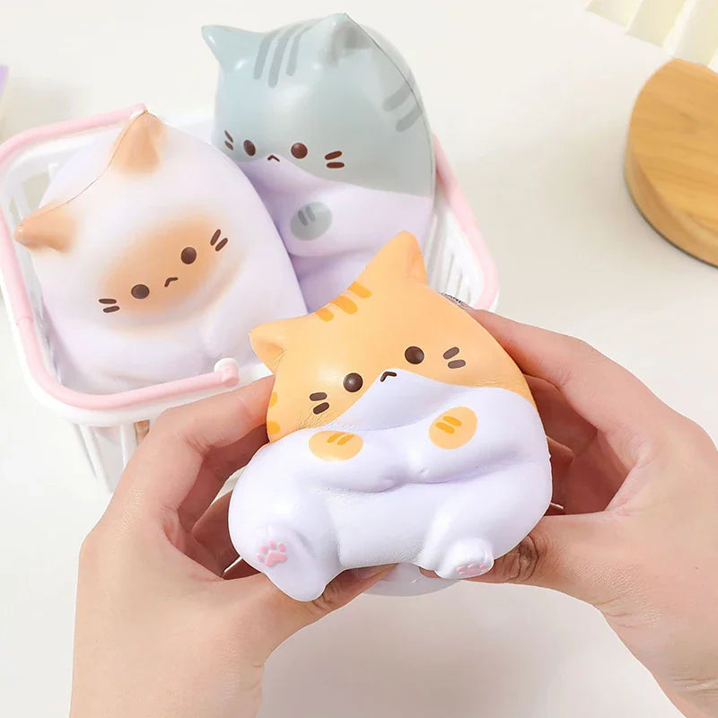 A hand squeezing a yellow and white cat stress relief toy with other toy cats in a small basket.