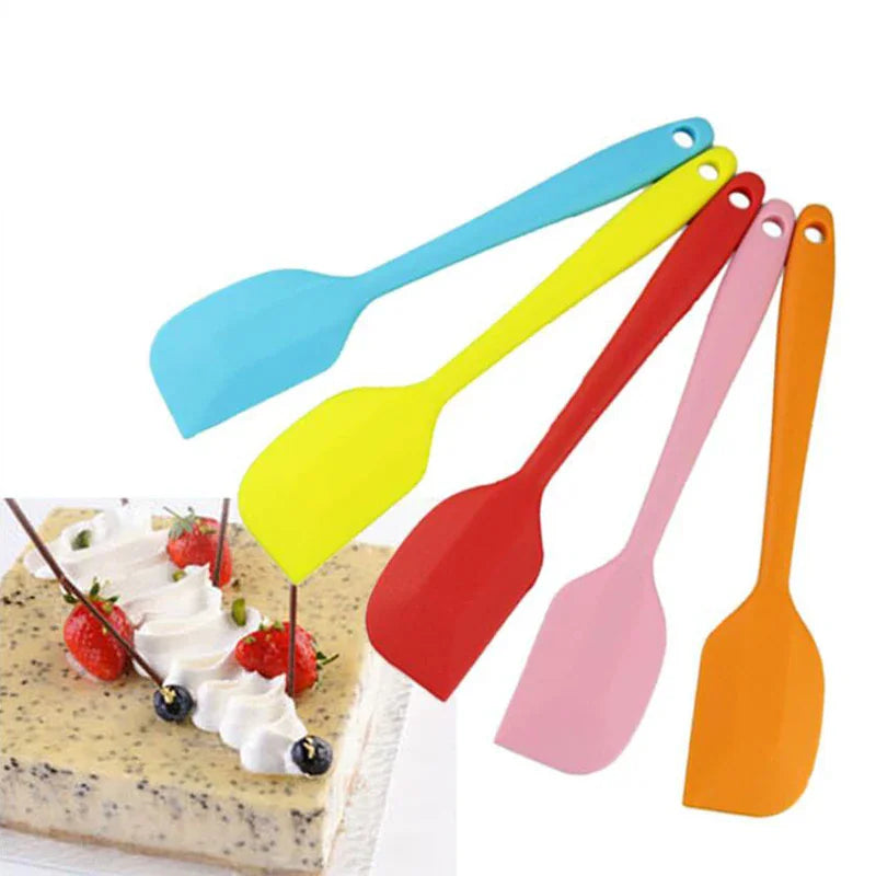 A set of five colorful silicone spatulas arranged next to a cake.