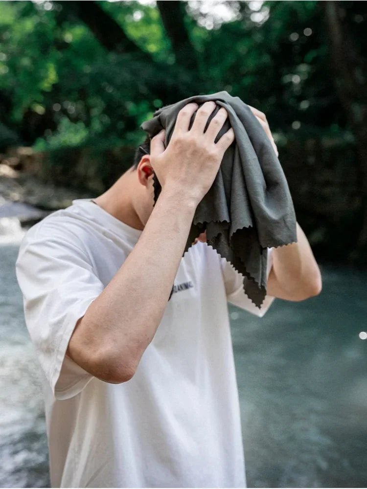 A person wiping their face or hair with a grey microfiber towel.