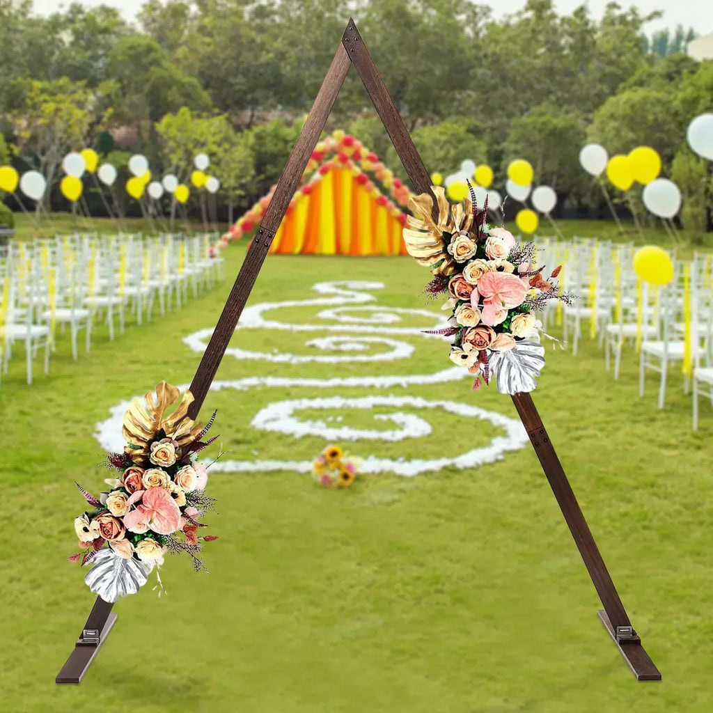 A wooden triangular wedding arch stand decorated with floral arrangements set up in an outdoor park setting.