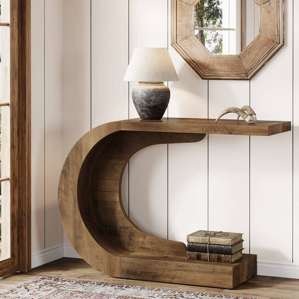 C-shaped rustic brown wooden console table in an entryway with a lamp and decor.