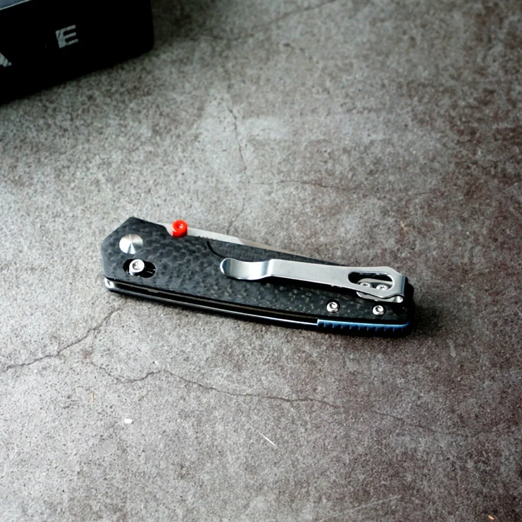 Closed tactical folding knife with a carbon fiber handle and red thumb stud