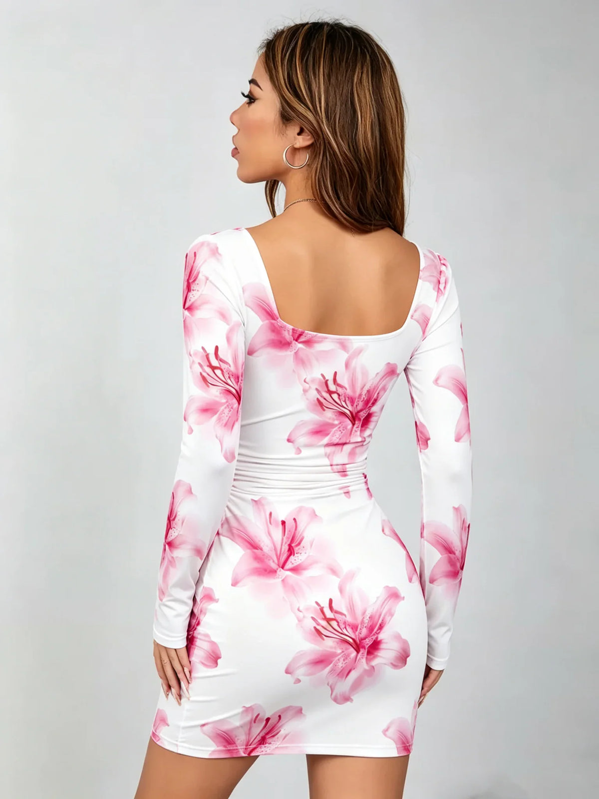 A back view of a woman wearing a white long-sleeve mini dress with a pink lily print.