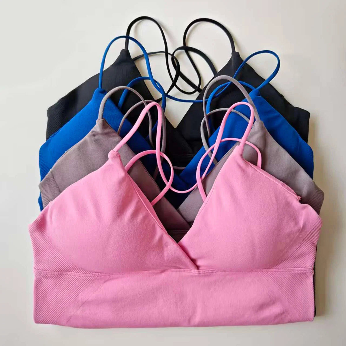 A stack of seamless workout tank tops in pink, grey, blue, and black with thin cross-back straps.