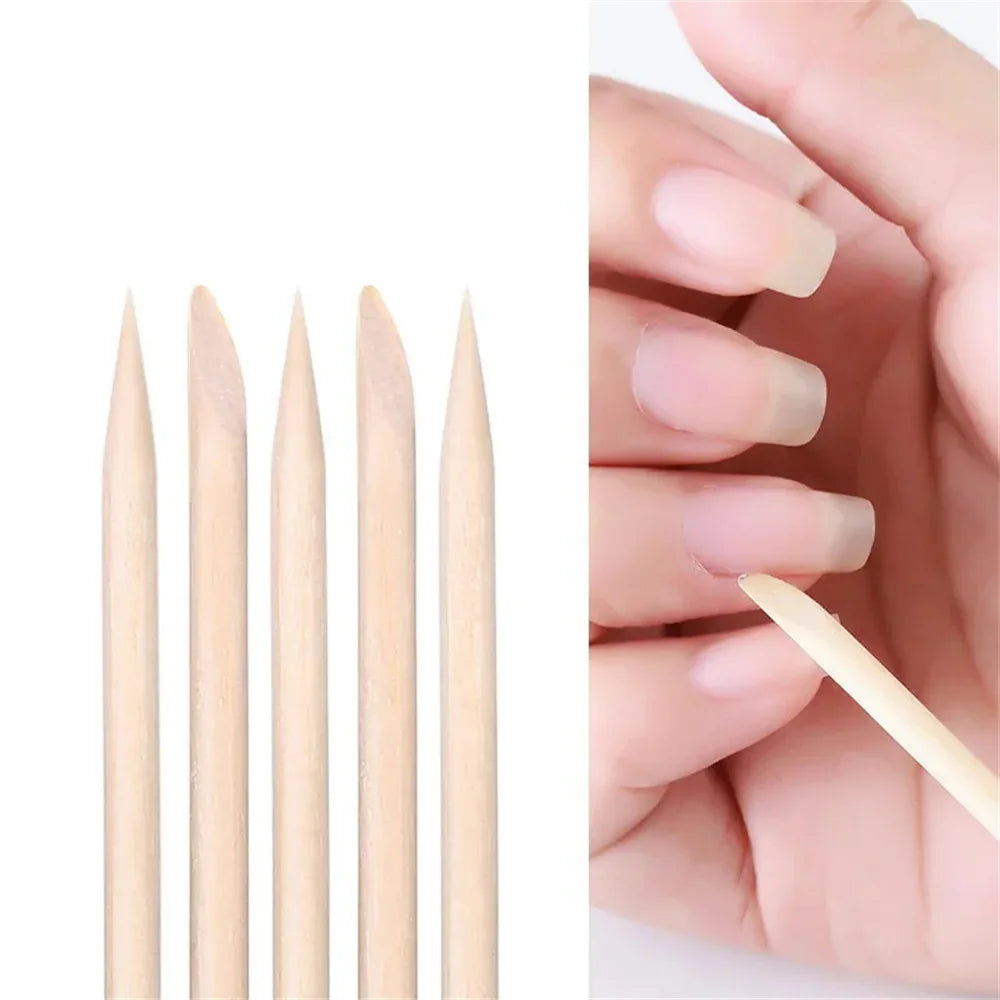 A close-up row of five wooden cuticle sticks next to a hand using one on a nail