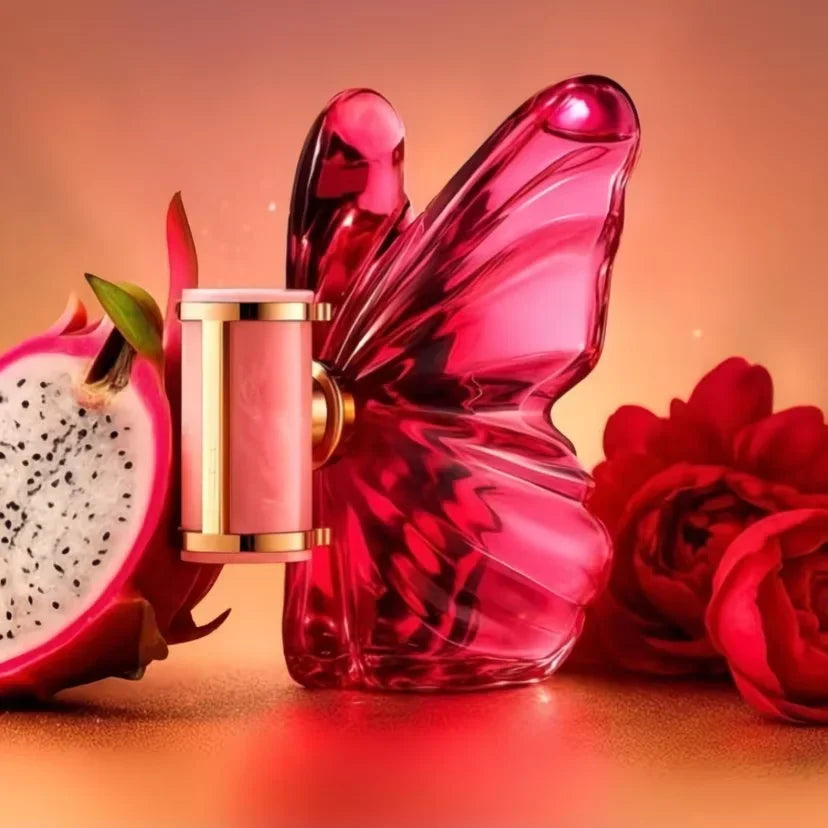 A pink butterfly-shaped glass perfume bottle next to a half dragon fruit and red rose flowers.