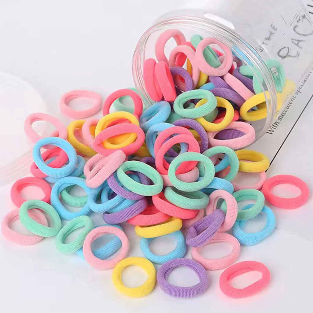 Assorted small seamless fabric hair elastics spilling out of a clear plastic jar