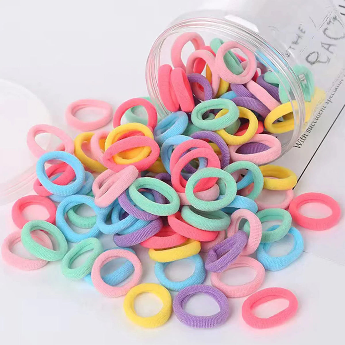 Assorted small seamless fabric hair elastics spilling out of a clear plastic jar