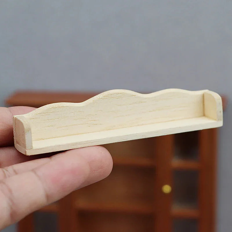 A small, light-colored wooden miniature dollhouse wall shelf held by a hand.