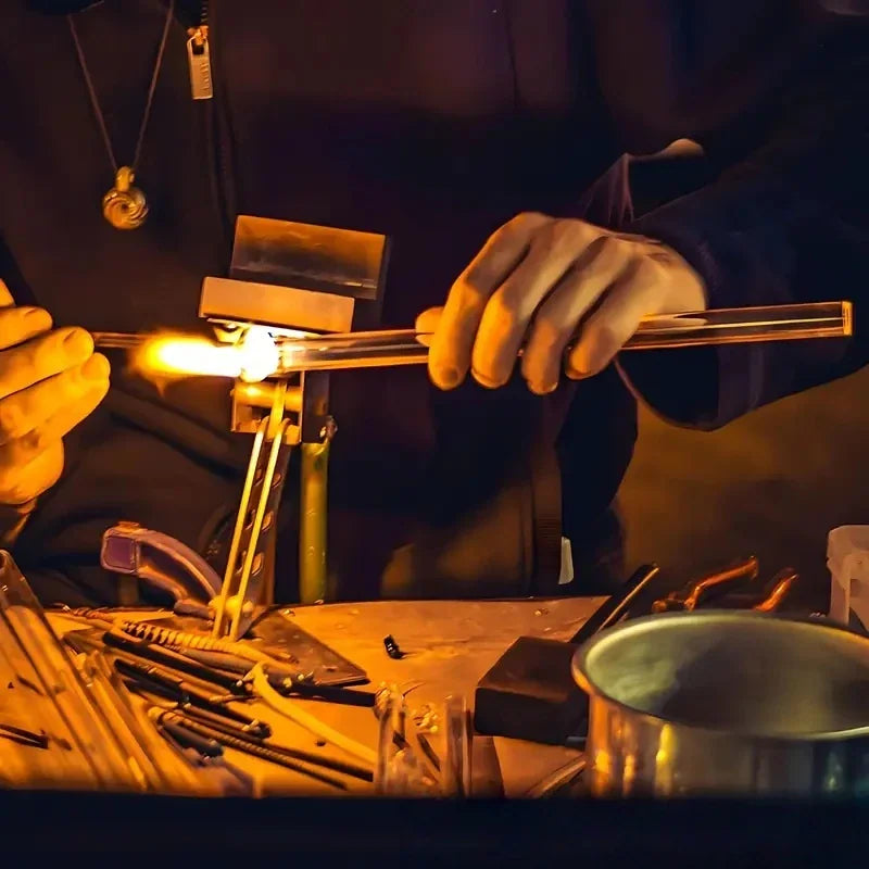 Close-up of a glassblower working on a glass tube with a torch.