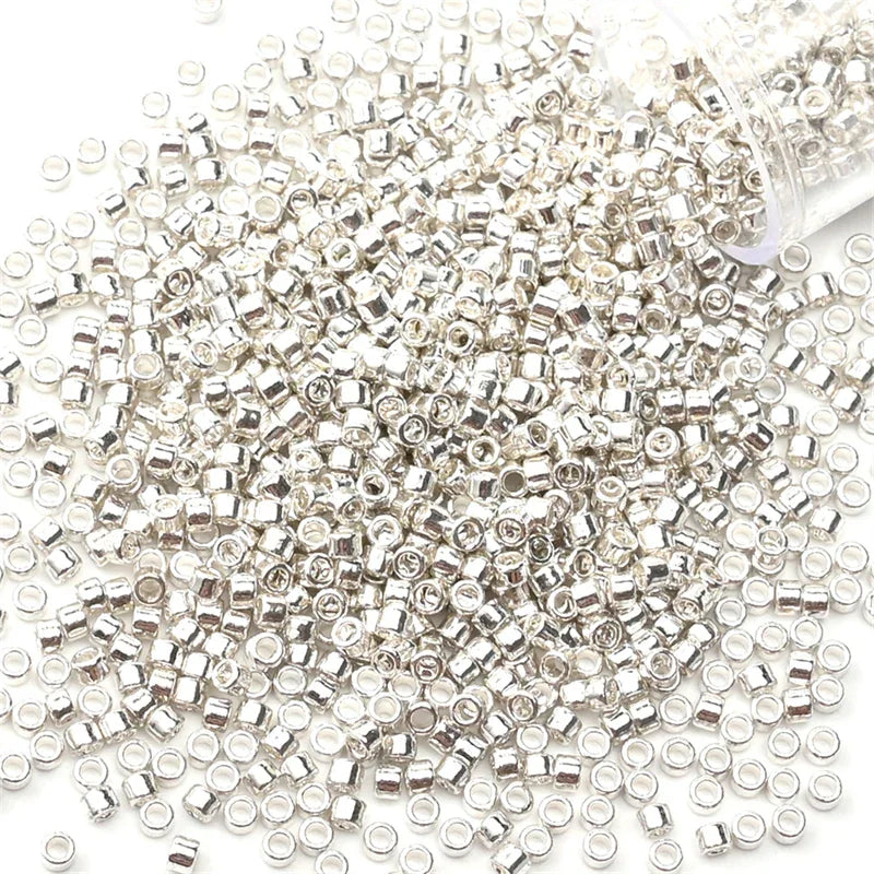 A pile of silver metallic glass seed beads next to a clear plastic container.