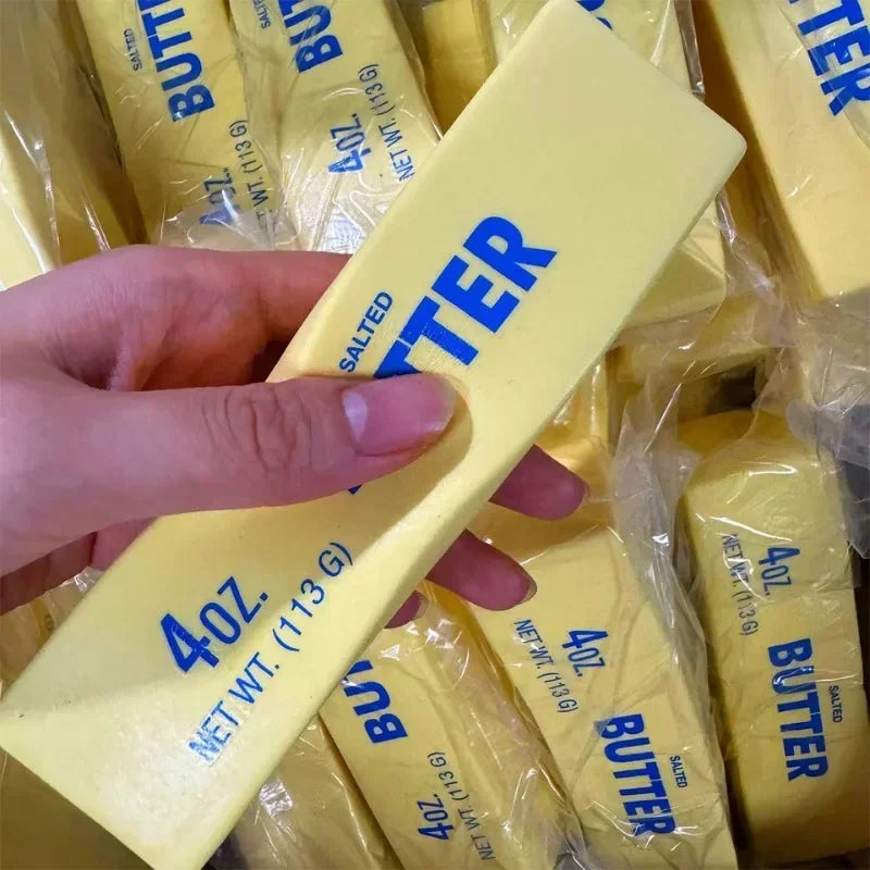Squishy yellow butter stick fidget toy held in hand with many others in background