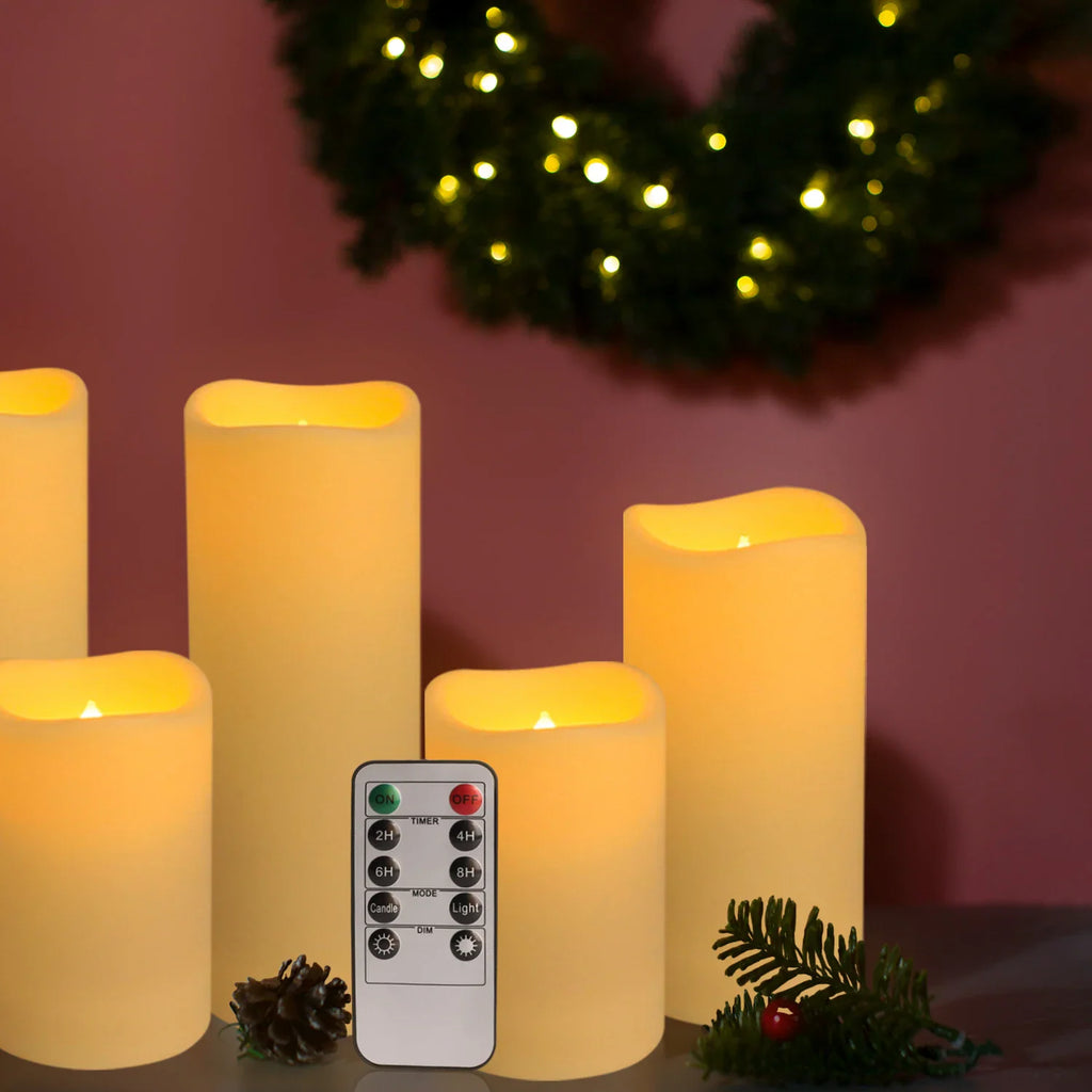 Flameless LED pillar candles with a remote control and decorative pine cone and green branch.