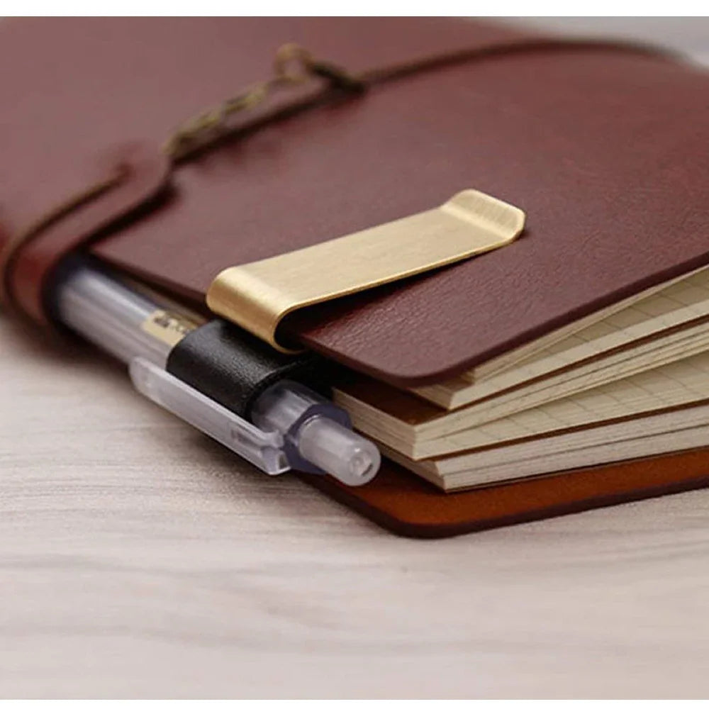 A metal and leather pen holder clip holding a pen on a brown notebook.