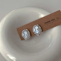 Irregular round pearl earrings with silver metal rims on a cardboard display card