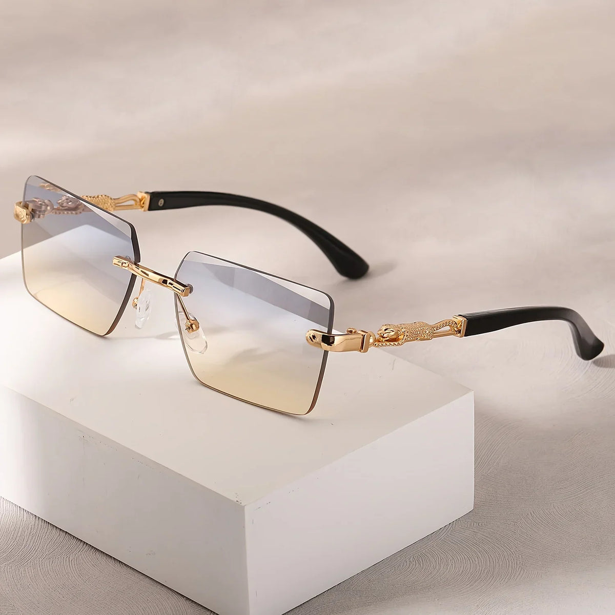 Rimless rectangular sunglasses with two-tone gradient lenses and gold panther-style metal temples on a white block