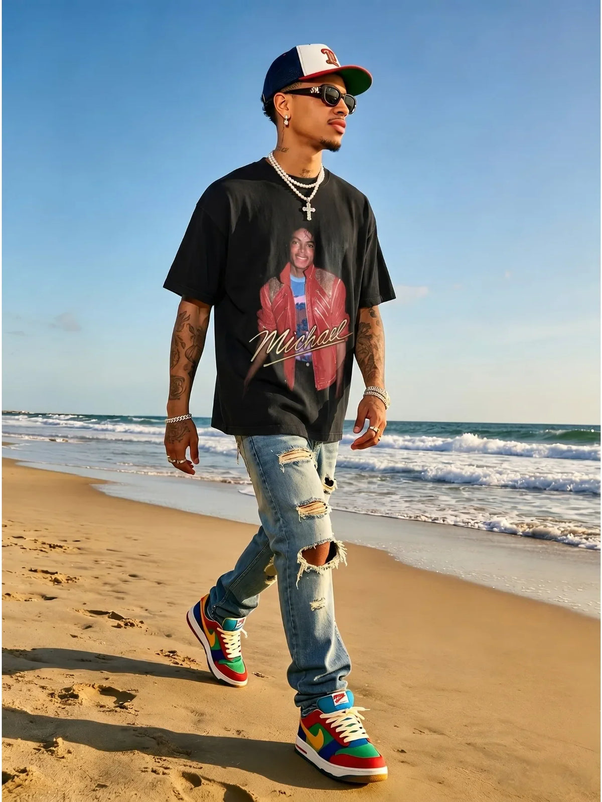 Man walking on a beach wearing a black graphic t-shirt, ripped jeans, sneakers, sunglasses, and a baseball cap