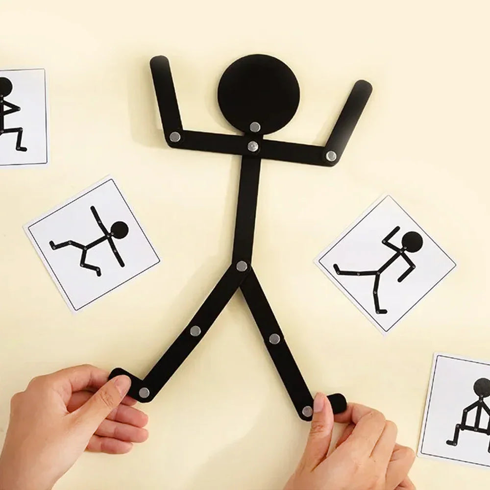 Hands demonstrating how to pose a black articulated wooden stick figure toy with reference cards on a tabletop.