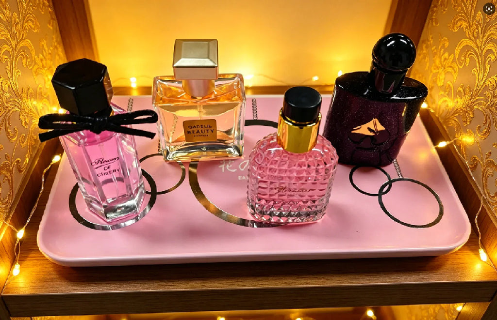 A gift set of four varied perfume bottles displayed on a pink decorative tray with warm fairy lights.