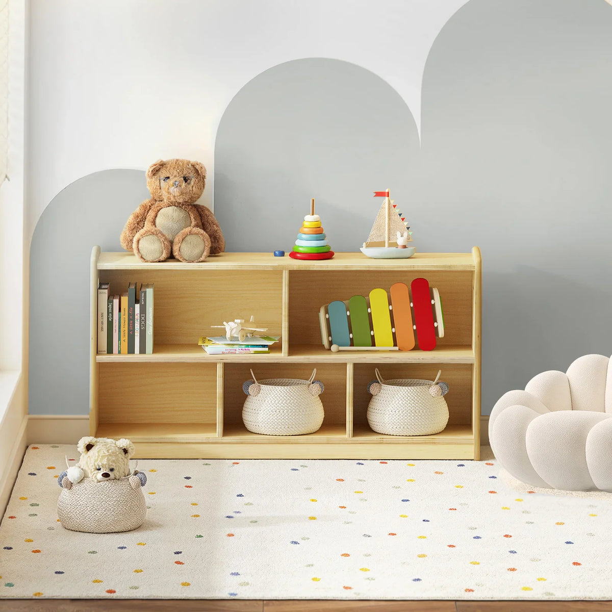 A light wood 2-tier Montessori toy storage cabinet in a playroom filled with books, baskets, and toys.