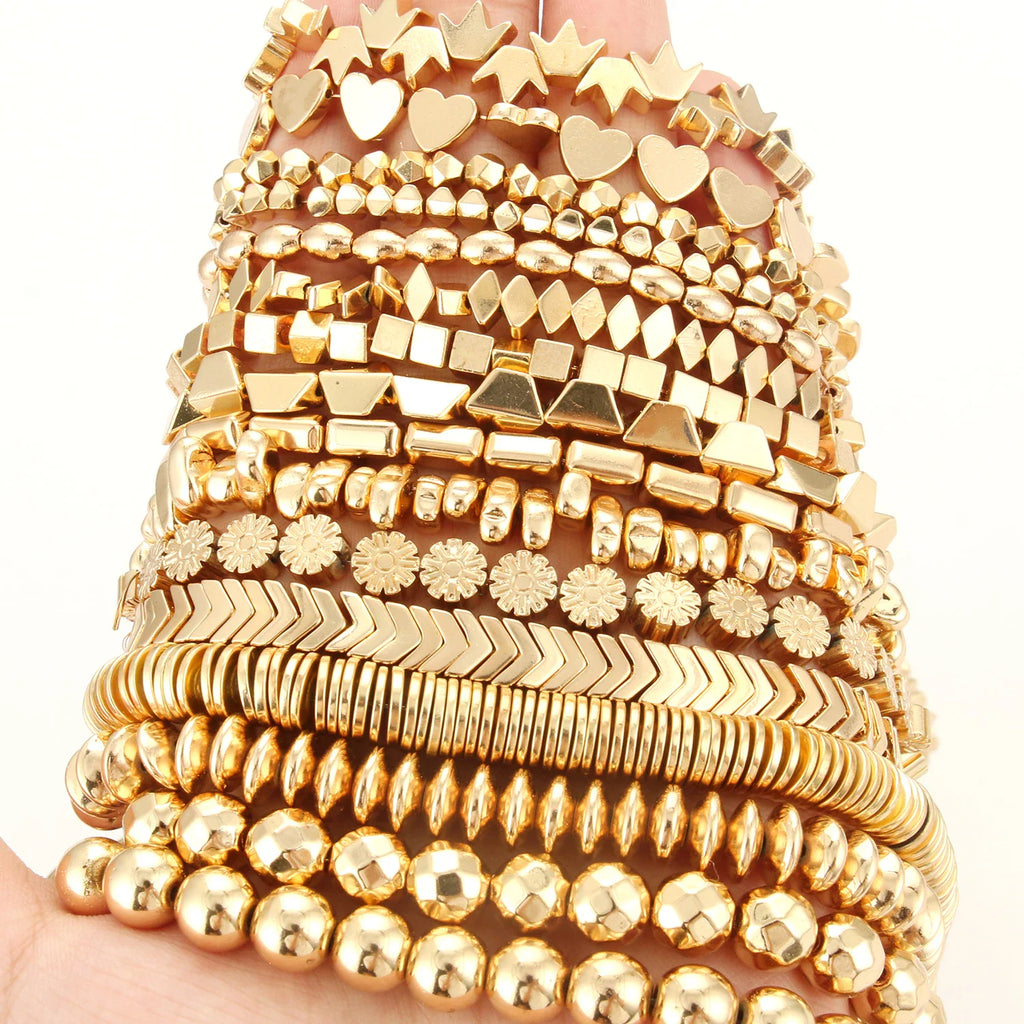 A hand holding a collection of various shaped gold-plated metal beads for jewelry making projects.