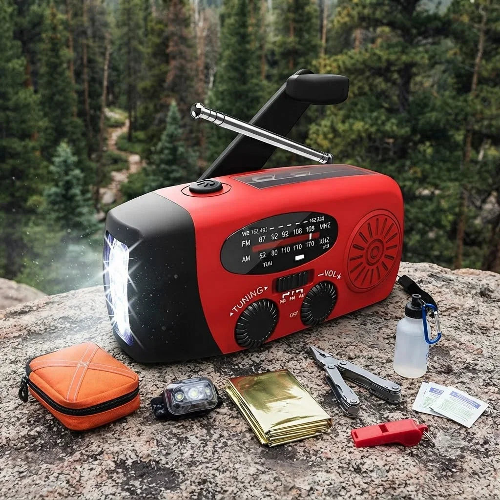 Portable red solar hand crank emergency radio with LED flashlight and various survival accessories on rock