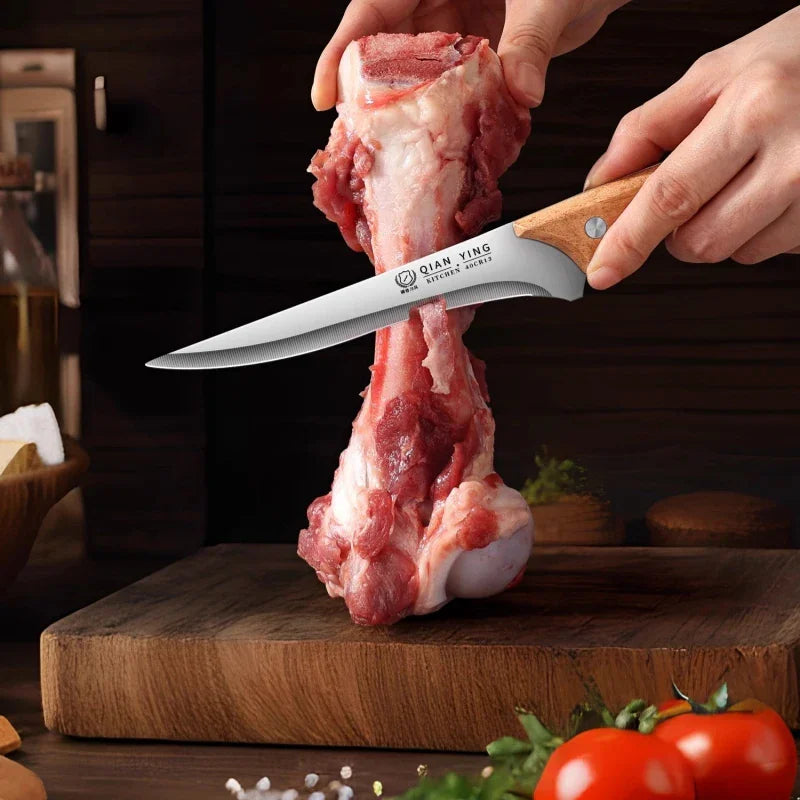 Close-up of hands using a stainless steel boning knife to cut a raw meat bone on a wooden board