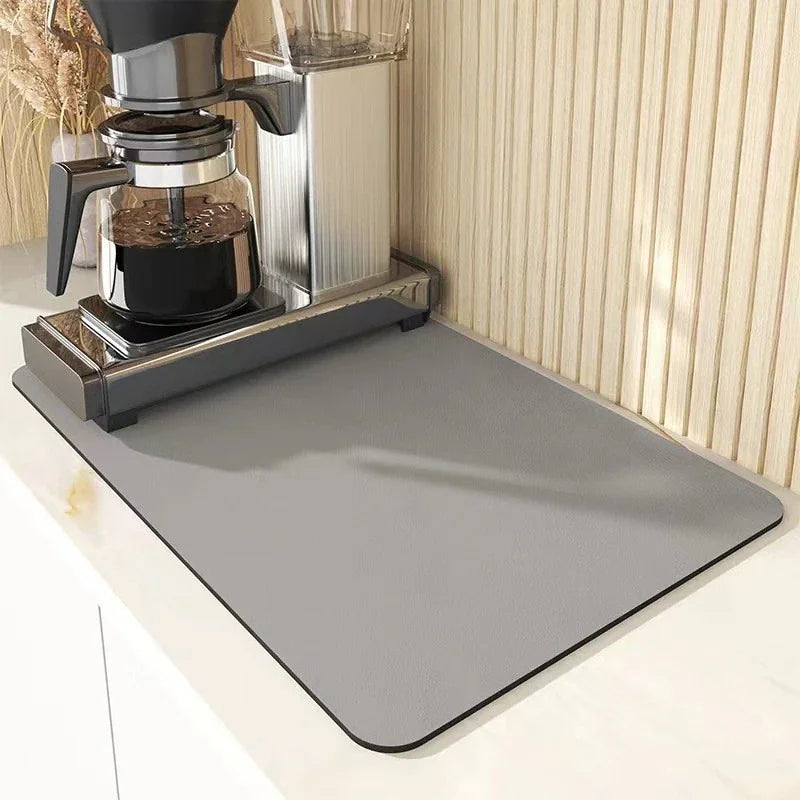 Grey absorbent kitchen drying mat under a coffee machine on a countertop.