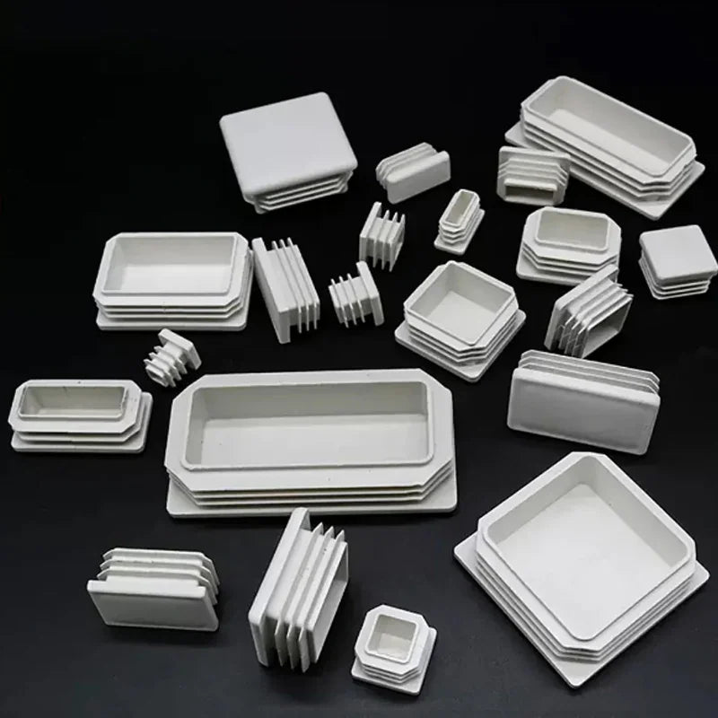 Collection of various sizes of white plastic square and rectangular tube end caps on black background