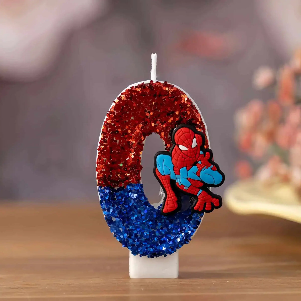 Number 0 birthday candle decorated with red and blue glitter and a cartoon superhero figure