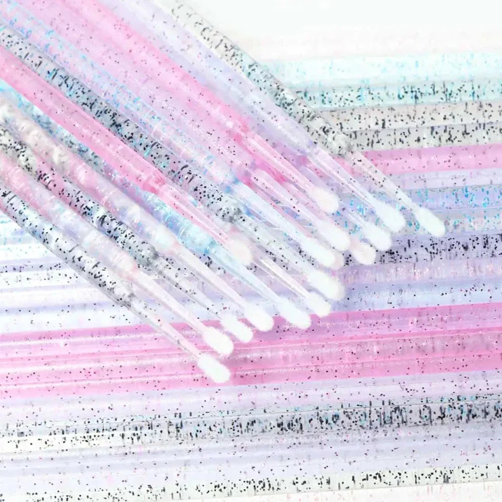 An assortment of colorful glittery disposable microbrushes with white tips for detailed beauty and lash applications.